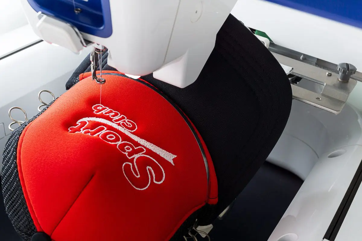 Embroidery machine stitching 'Sport' on red fabric.