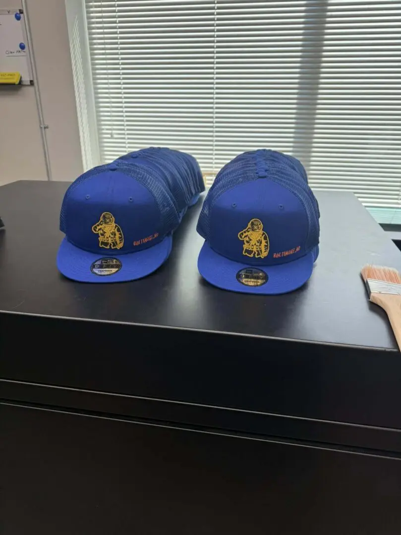 Two stacks of blue baseball caps with a yellow emblem on a black desk.