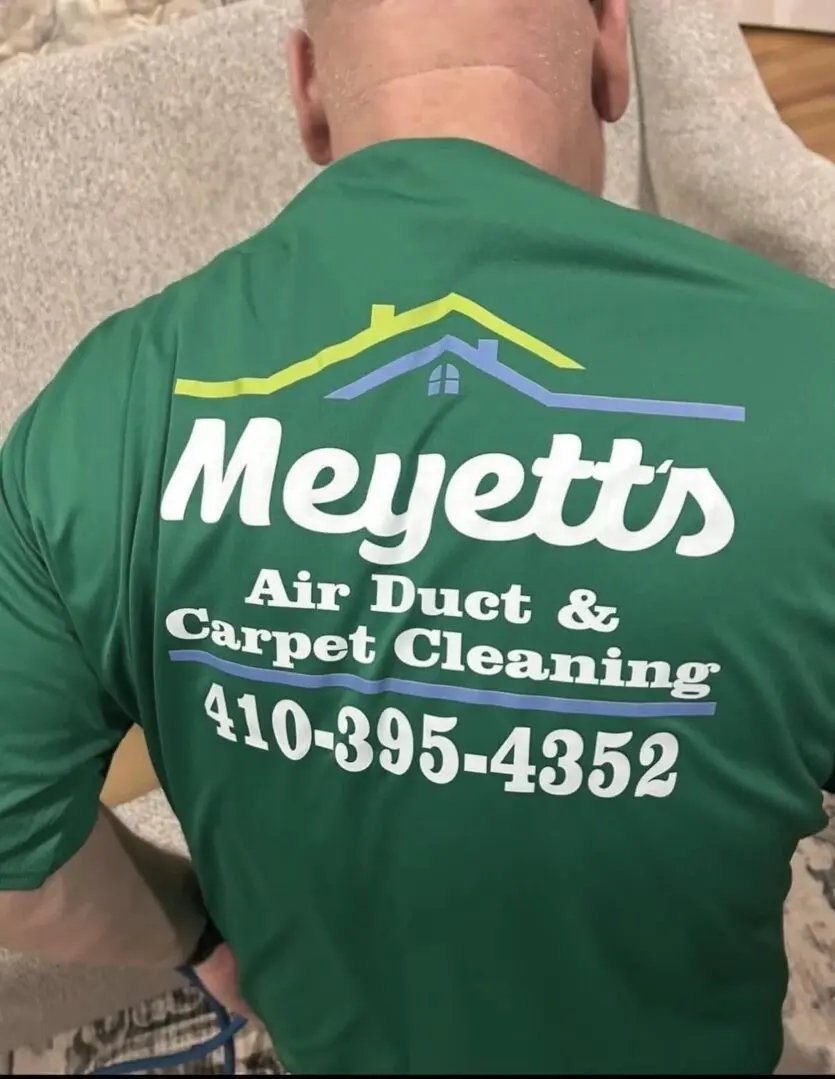 Back of a green shirt advertising Meyett's Air Duct & Carpet Cleaning with phone number.