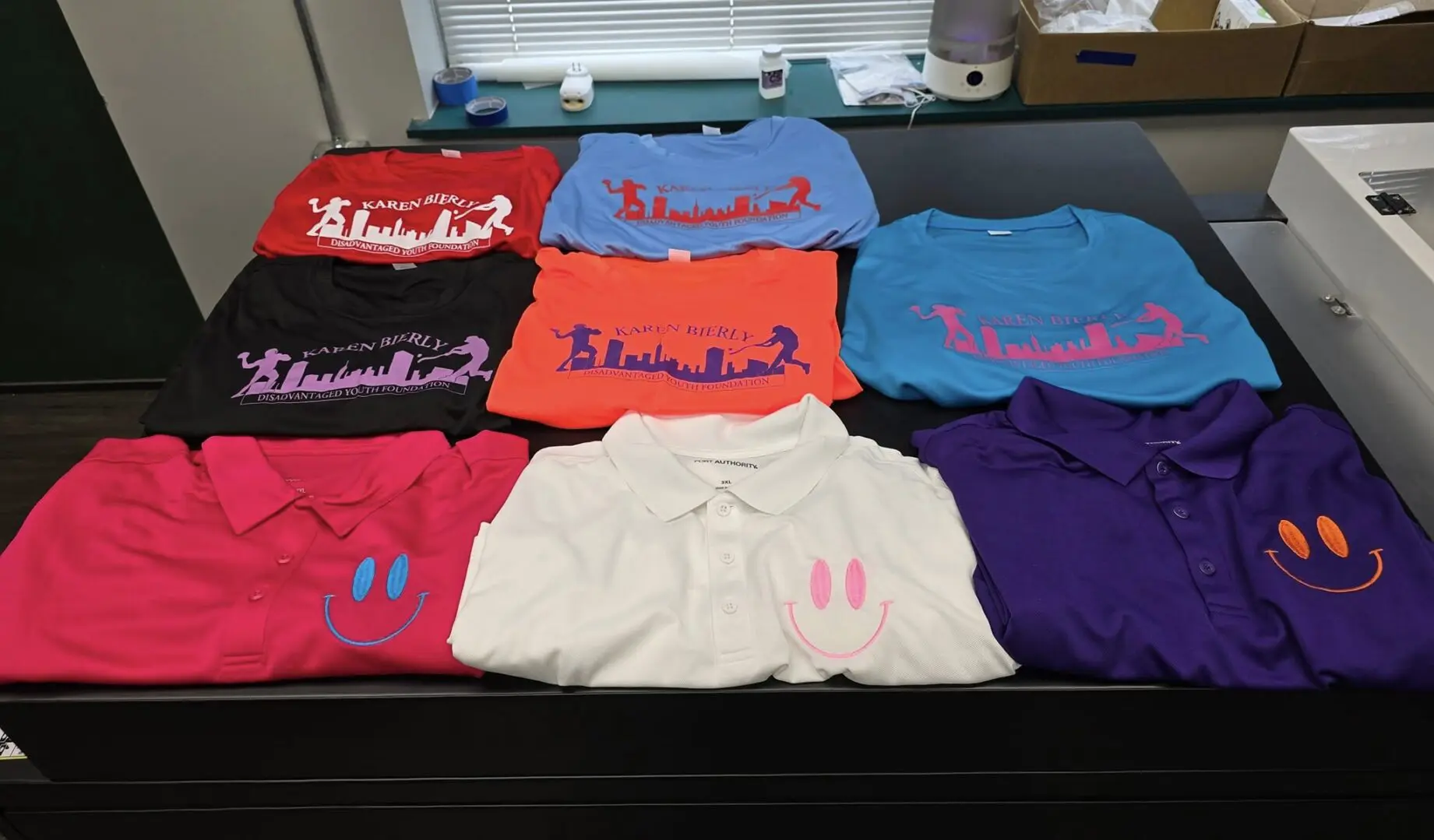 Nine colorful shirts with varied logos neatly arranged on a table.