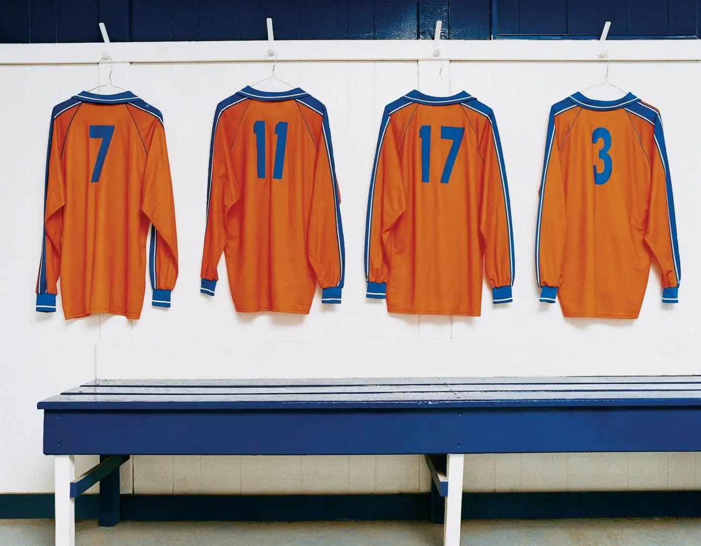 Orange sports jerseys numbered 7, 11, 17, and 3 hanging on hooks.