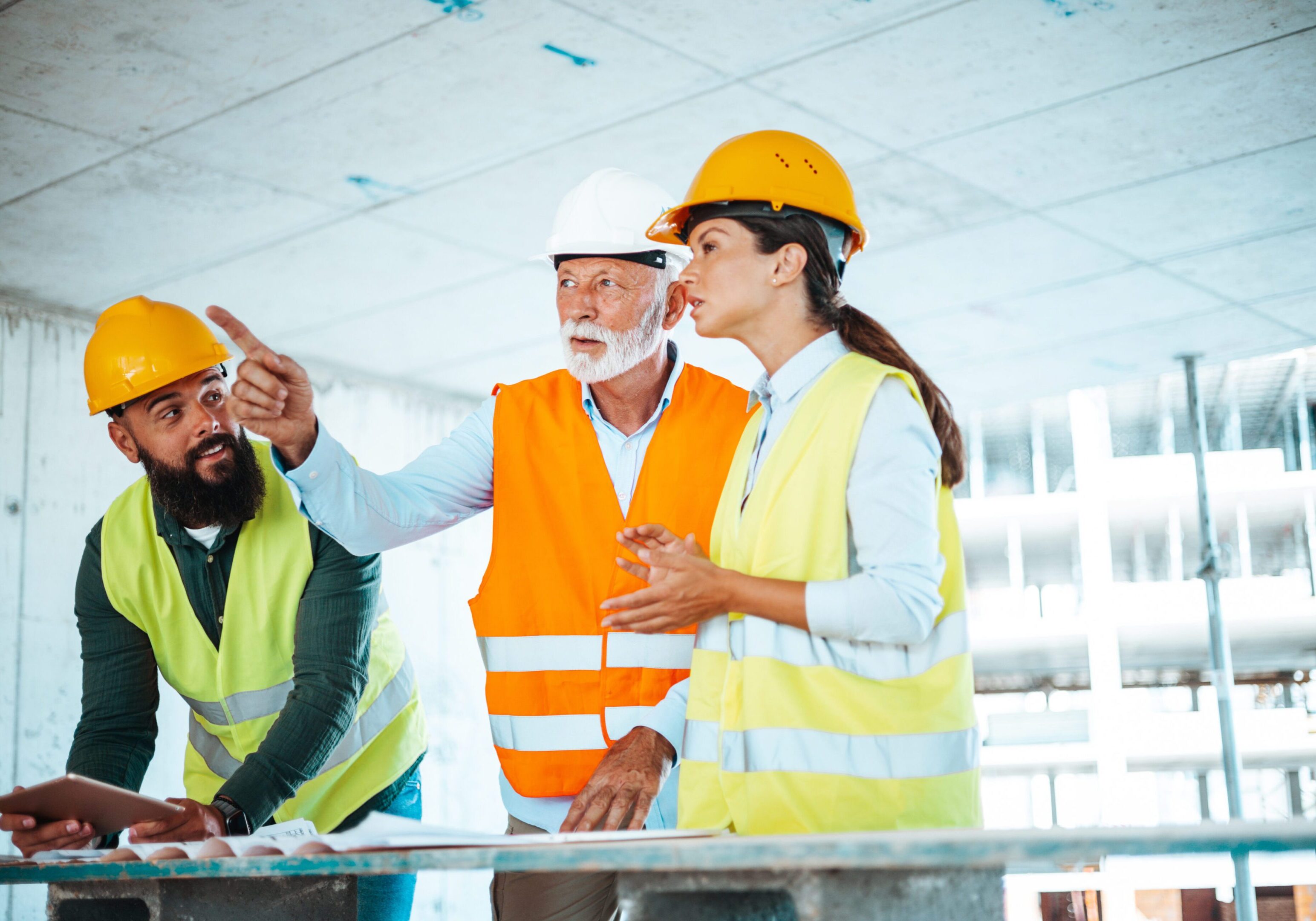 Construction workers discussing plans on site, wearing safety gear.